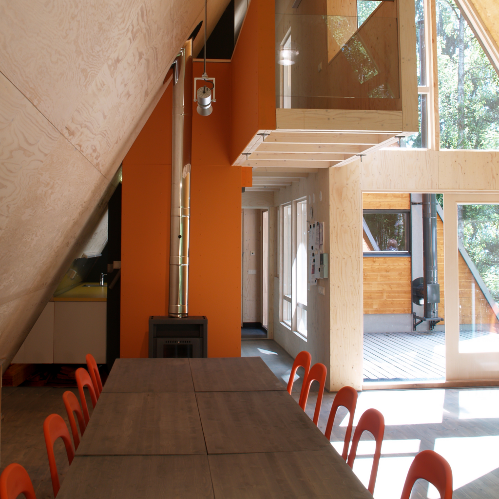 Kuvassa moderni kerhotila. Ruokapöytä ja oransseja tuoleja.